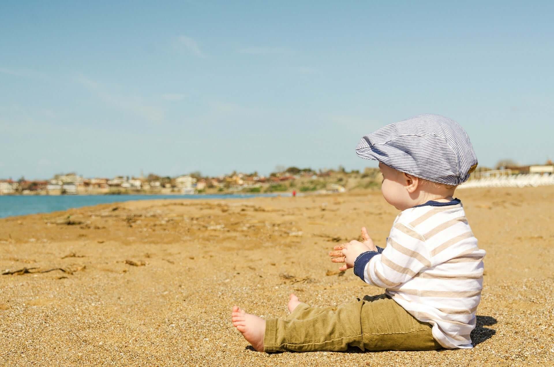 Baby sitting on the beach enjoying the sand and water on a sunny day.